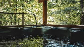 A hot tub with a view of a forest through a window.