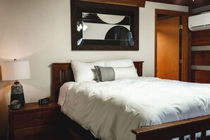 Een net opgemaakt bed met witte beddengoed, een bedlampje en een digitale klok op een nachtkastje van hout.