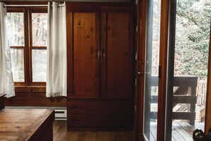 Een kamer met houten vloeren, een grote kast, een bankje en een raam met gordijnen.