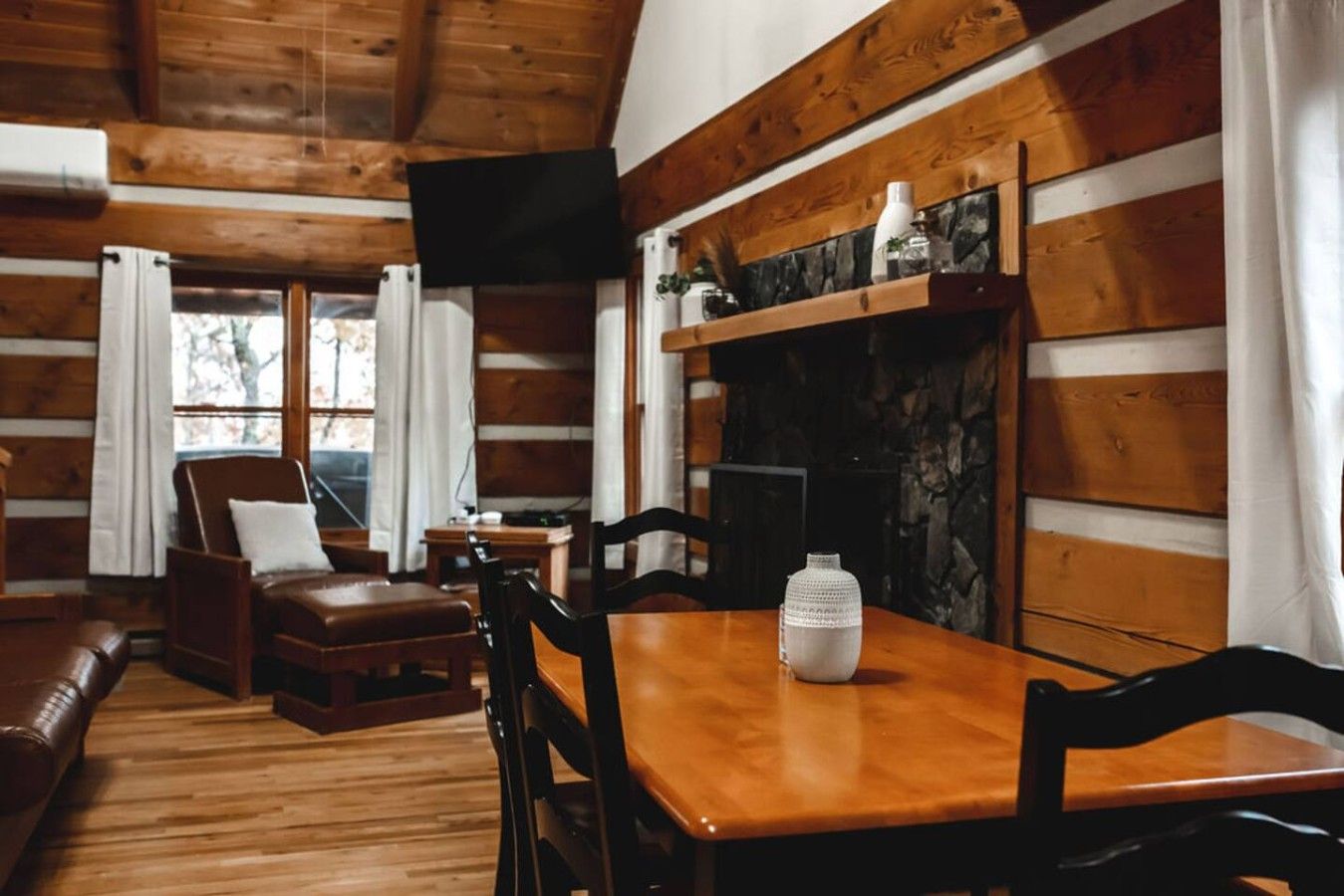 L’intérieur chaleureux d’un chalet avec une table à manger en bois, des chaises, un canapé et une cheminée.