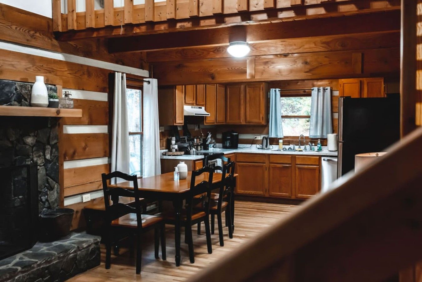 Interior de una cabaña con comedor, cocina y chimenea de piedra.
