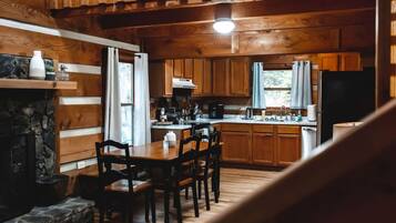 Interior de una cabaña con comedor, cocina y chimenea de piedra.