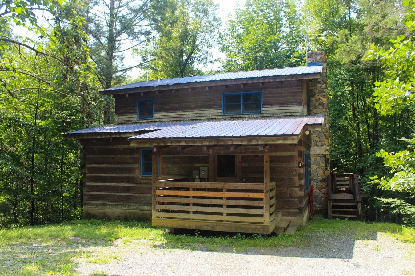 Une cabane en bois rustique, dotée d’un porche et d’une cheminée en pierre, entourée d’une forêt dense.
