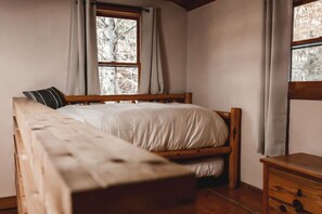 Een eenpersoonsbed met houten frame en witte beddengoed in een kamer met raam en een nachtkastje van hout.