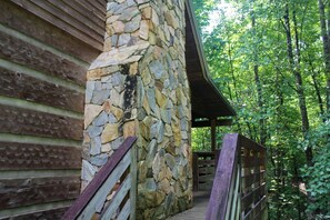 Un bâtiment en pierre doté d’une terrasse en bois et d’une allée couverte, le tout entouré d’arbres.