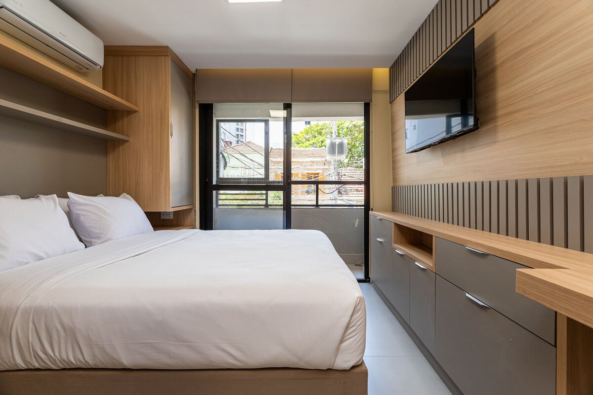 A modern bedroom with a bed, built-in TV, and a view of the outside.