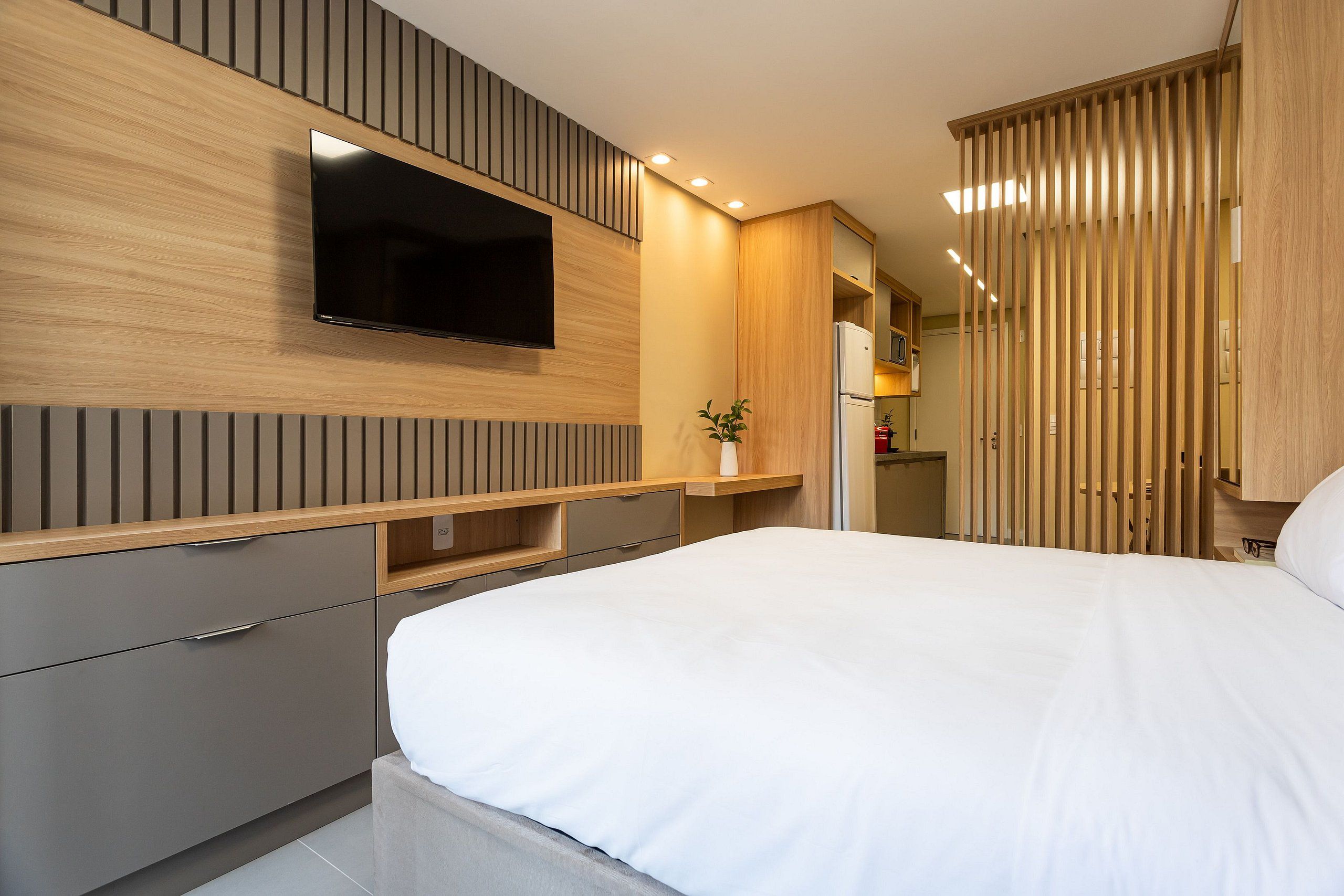 A modern bedroom with a flat-screen TV mounted on the wall, a bed with white bedding, and built-in wooden cabinets.