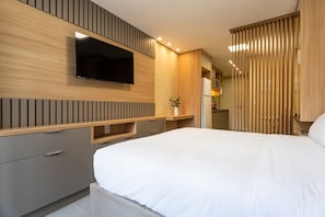 Ein modernes Schlafzimmer mit einem an der Wand befestigten Flachbildfernseher, einem Bett mit weißer Bettwäsche und eingebauten Holzausbau.