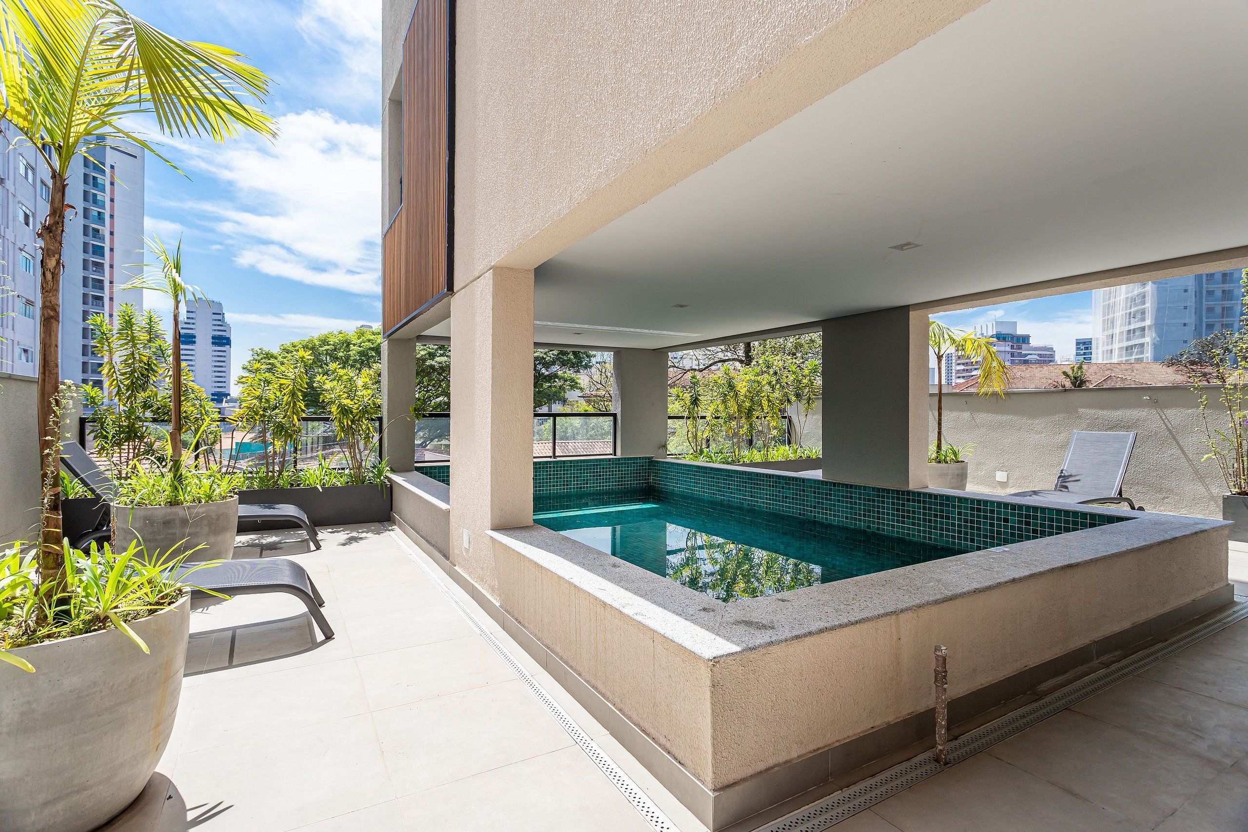 A rooftop swimming pool with a view of the cityscape, surrounded by potted plants and outdoor seating.