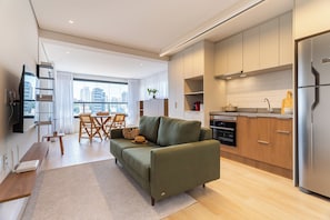 A modern apartment with a green sofa, dining area, kitchen, and a city view. - Equalize Vila Mariana by Viva (São Paulo)