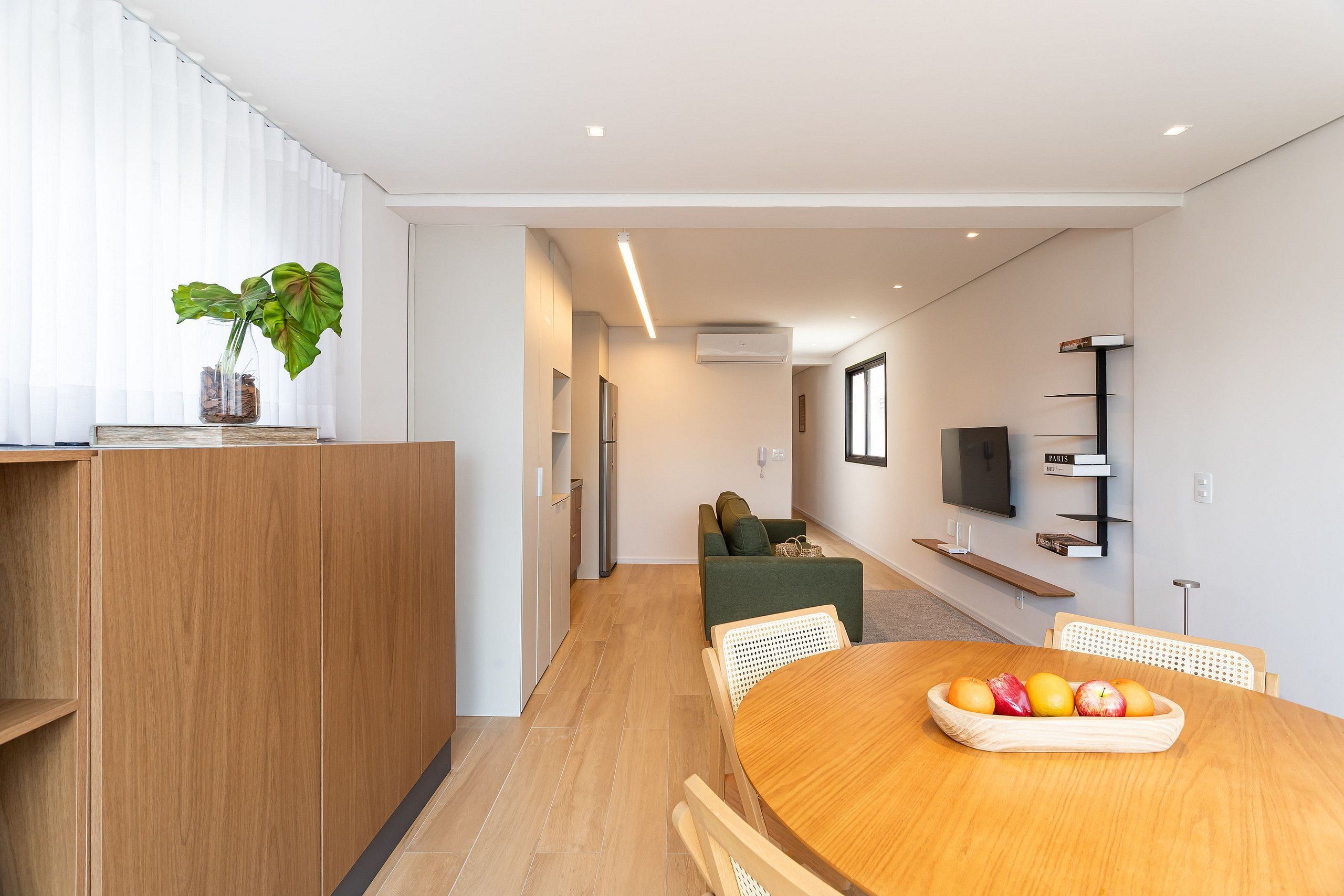Un salon moderne avec une table à manger en bois, un canapé et un téléviseur fixé au mur.
