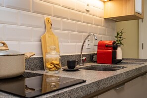 A kitchen with a granite countertop, a wooden cutting board, a glass jar of cookies, a coffee maker, and a black mug. - Equalize Vila Mariana by Viva (São Paulo)