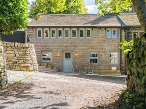 A stone building with a central entrance, multiple windows, and a gravel driveway. - Heaven Lea Cottage (Oldham)