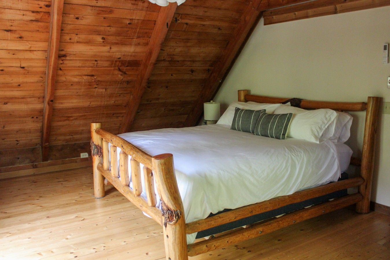 Un lit à ossature en bois dans une pièce dont le plancher et le plafond sont en bois, ce dernier étant incliné.