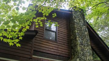 A cabin with a stone chimney, wooden siding, and a window.