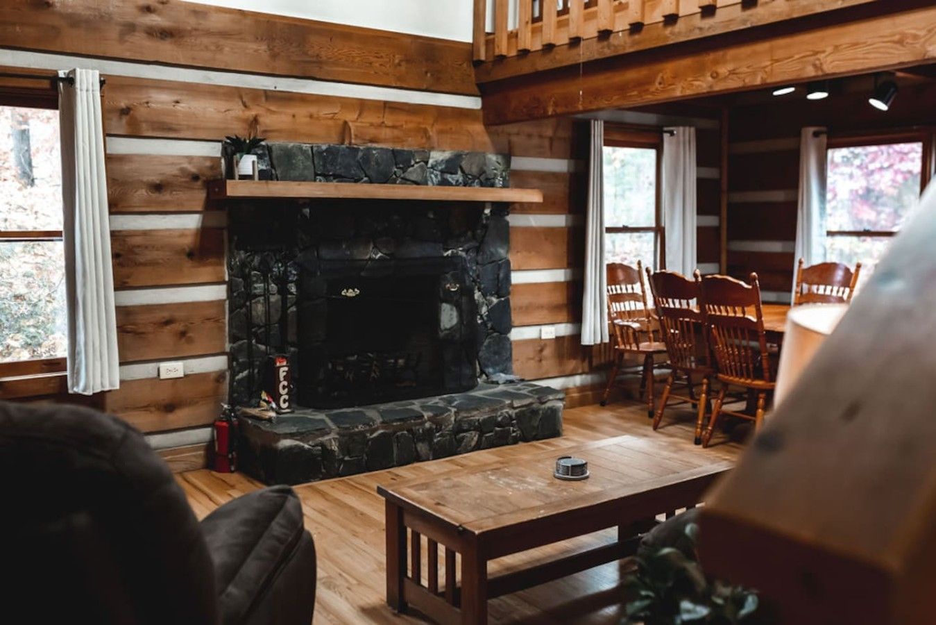 A cozy room with a stone fireplace, wooden walls, and a dining area with chairs.