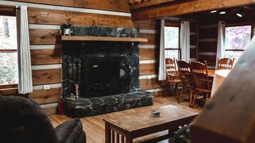 A cozy room with a stone fireplace, wooden walls, and a dining area with chairs.