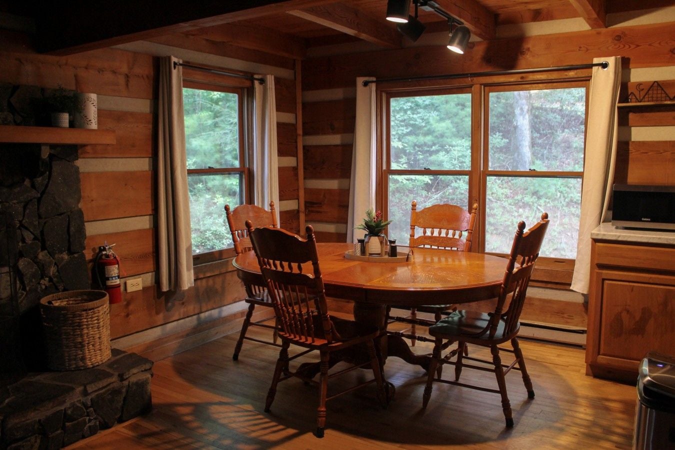 Un intérieur en bois avec une table de salle à manger ronde, quatre chaises et de grandes fenêtres donnant sur la forêt.