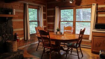 Un intérieur en bois avec une table de salle à manger ronde, quatre chaises et de grandes fenêtres donnant sur la forêt.