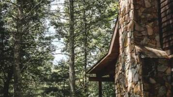Un bâtiment en pierre avec un escalier en bois menant à une terrasse, le tout entouré de grands arbres.