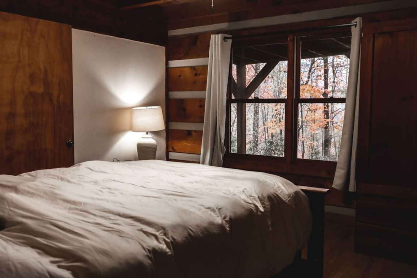 A bedroom with a bed, a nightstand, a lamp, and a window with a view of trees.