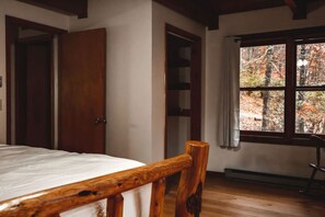 Een slaapkamer met een houten bedframe, een kledingkast, een raam met uitzicht op bomen en een radiator.