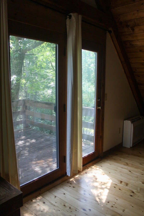 Een kamer met een houten vloer, een schuifdeur naar een terras buiten, en een wit apparaat in de hoek.