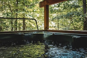 Een hottub met houten rand en uitzicht op een bos door een raam.