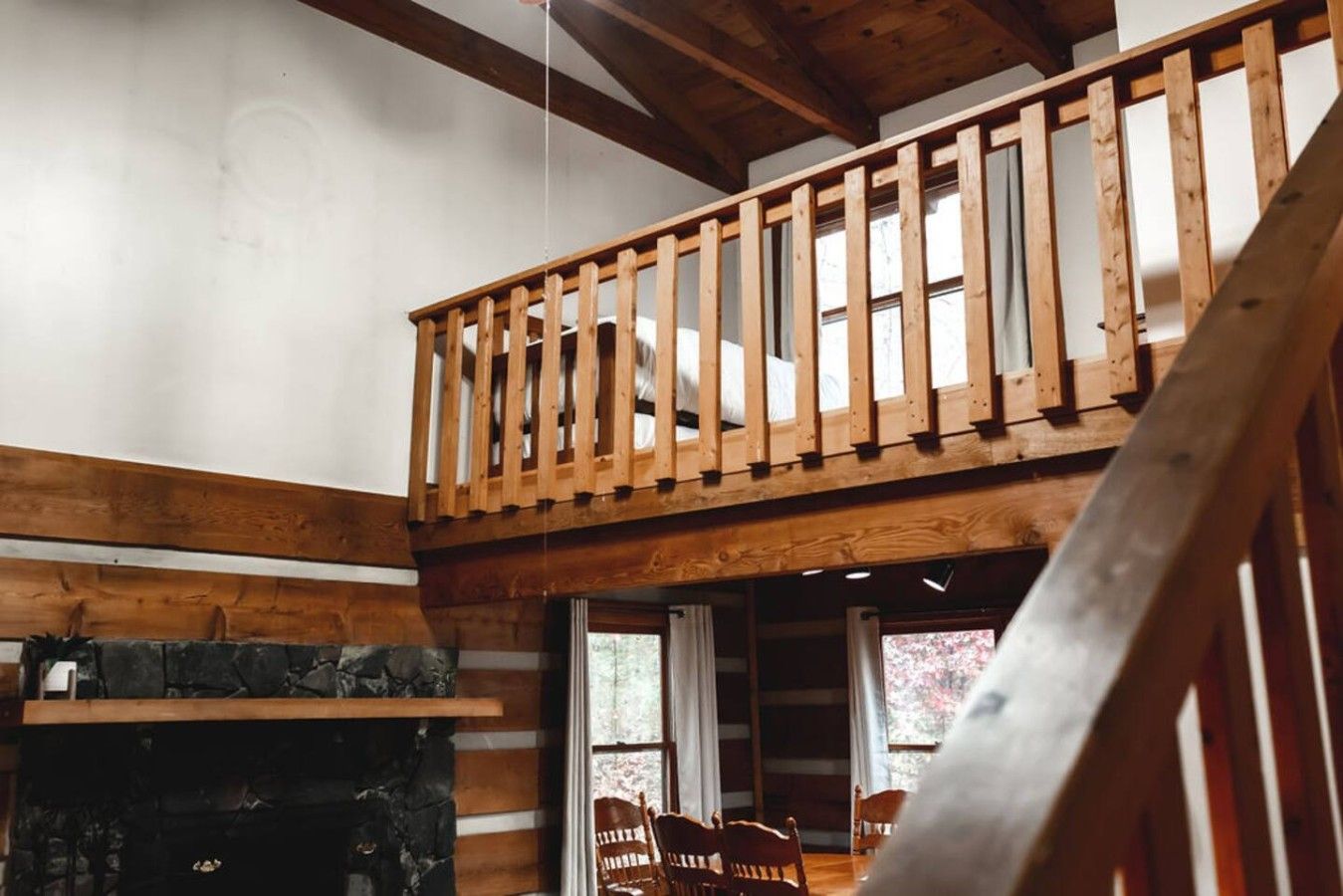 A wooden staircase leading to a loft bedroom with a stone fireplace and a view of the outdoors.
