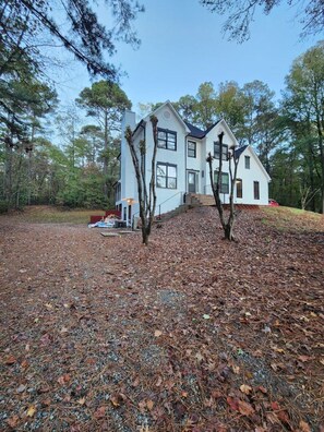 A two-story white house with a dark roof, surrounded by trees and a leaf-covered ground. - The Quiet Studio, lux apartment, in central area. (Newnan)