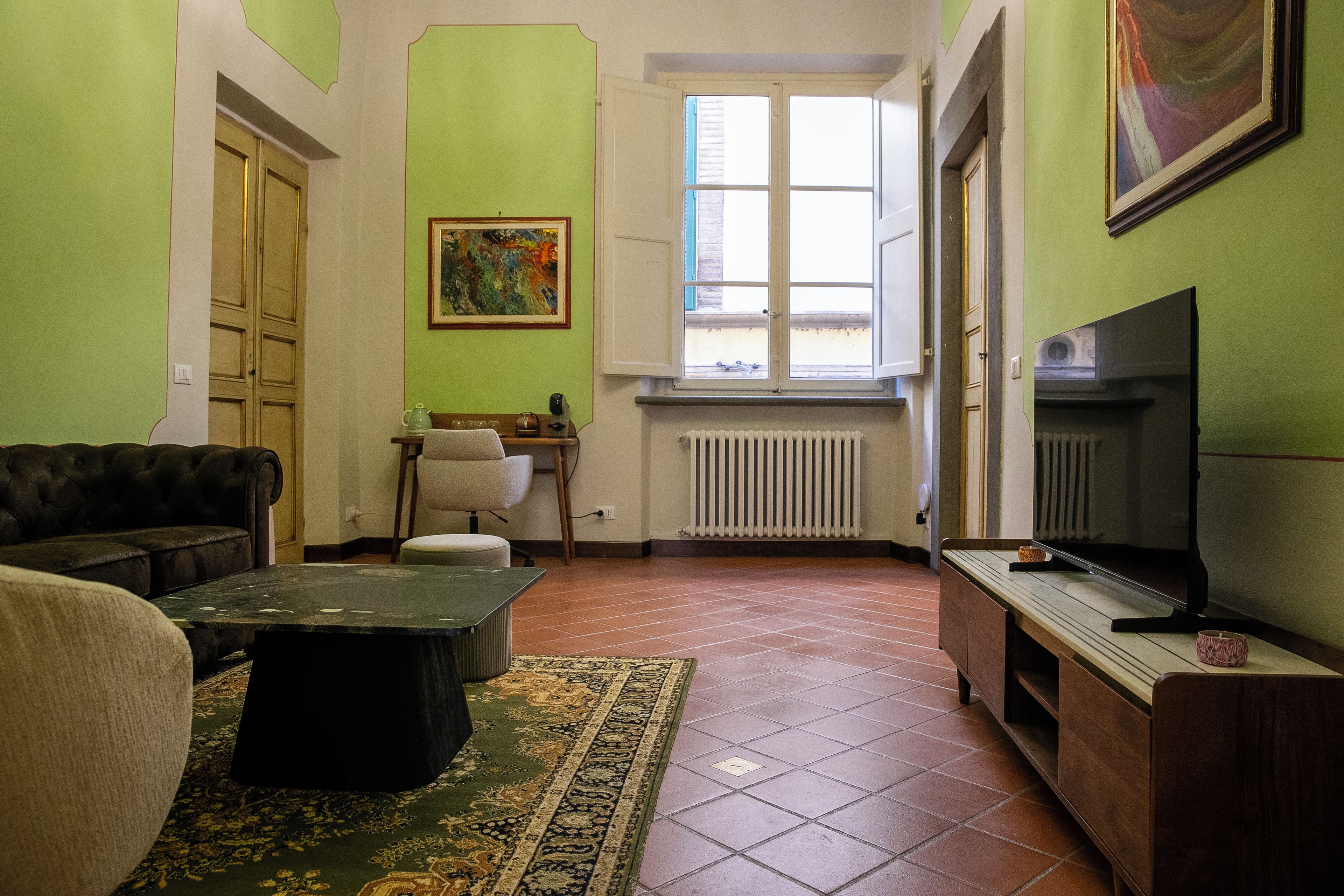 A living room with a sofa, a coffee table, a TV, a radiator, and a window with a view.