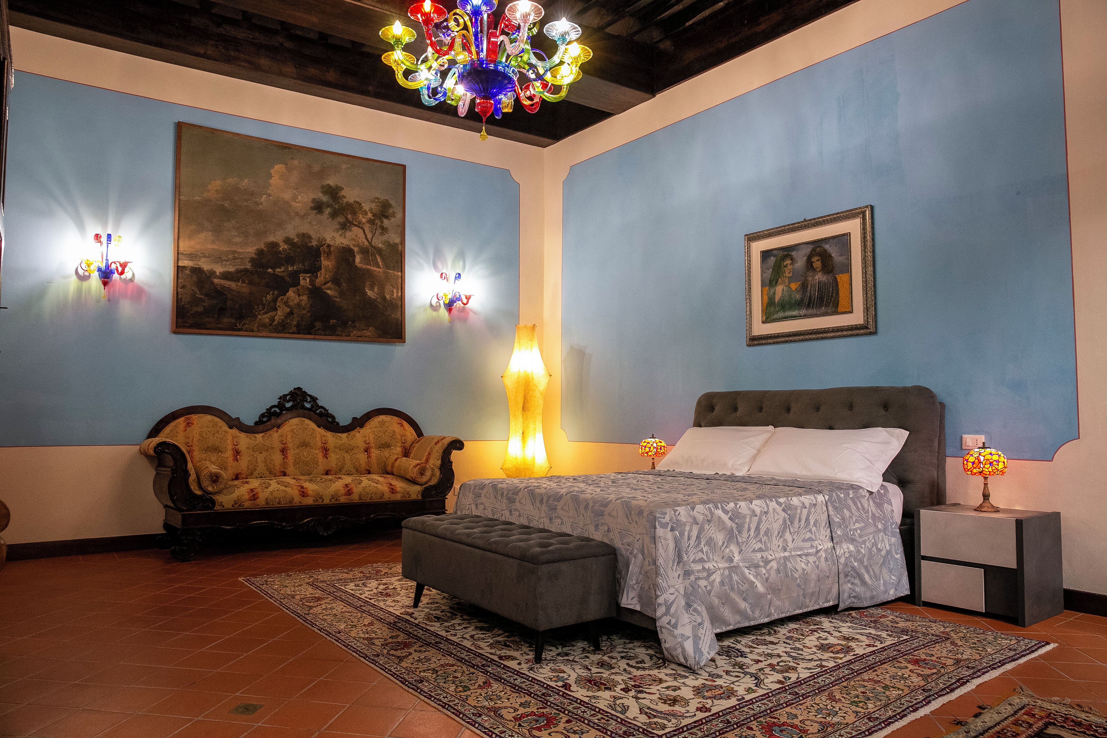 A bedroom with a bed, a sofa, a nightstand, a lamp, and a painting on the wall.