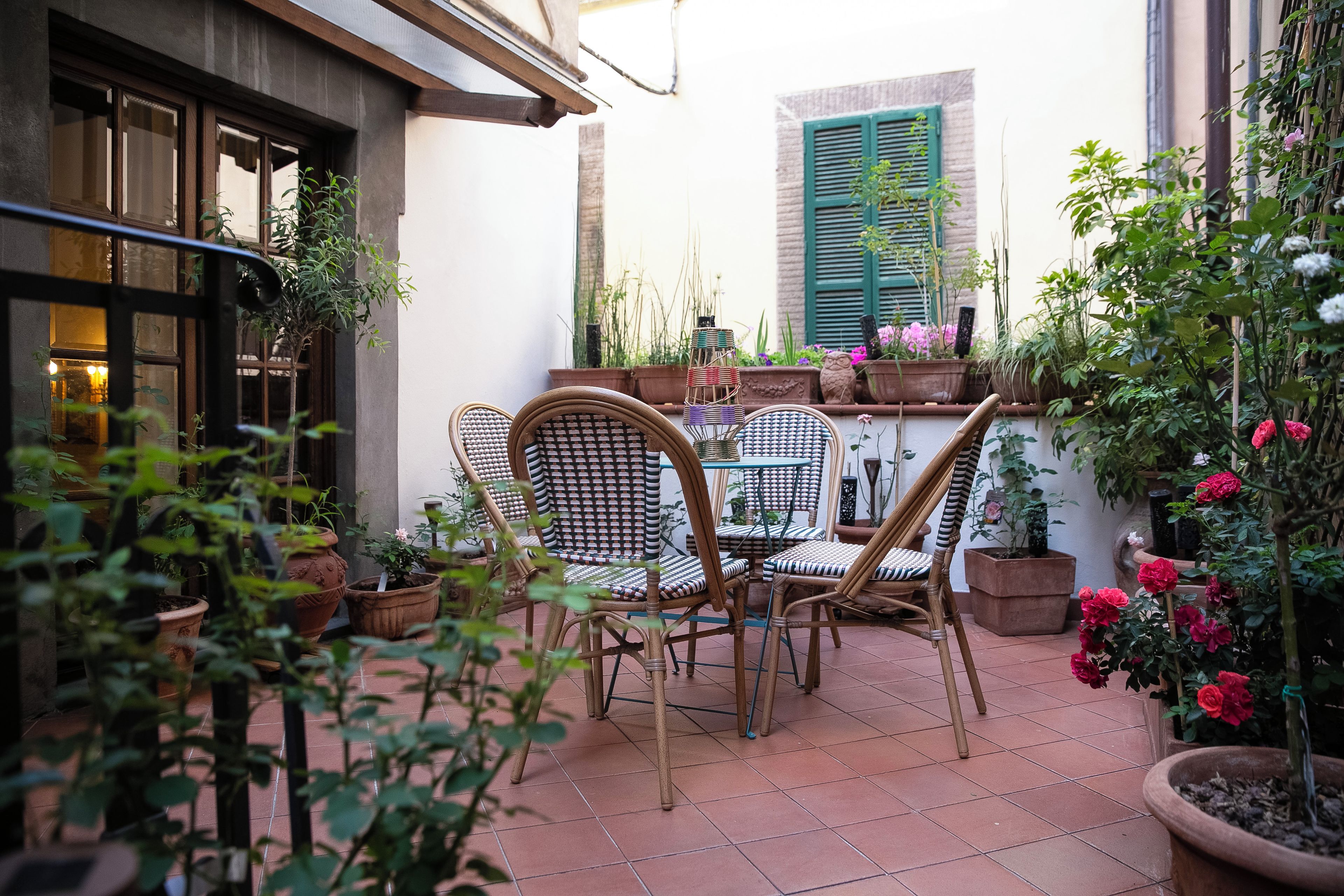 Ein Terrassenbereich im Freien mit Tisch und Stühlen, umgeben von Kübelpflanzen und Blumen.