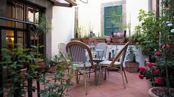 Ein Terrassenbereich im Freien mit Tisch und Stühlen, umgeben von Kübelpflanzen und Blumen.