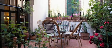 Un área de patio al aire libre con una mesa y sillas, rodeada de plantas y flores en macetas.