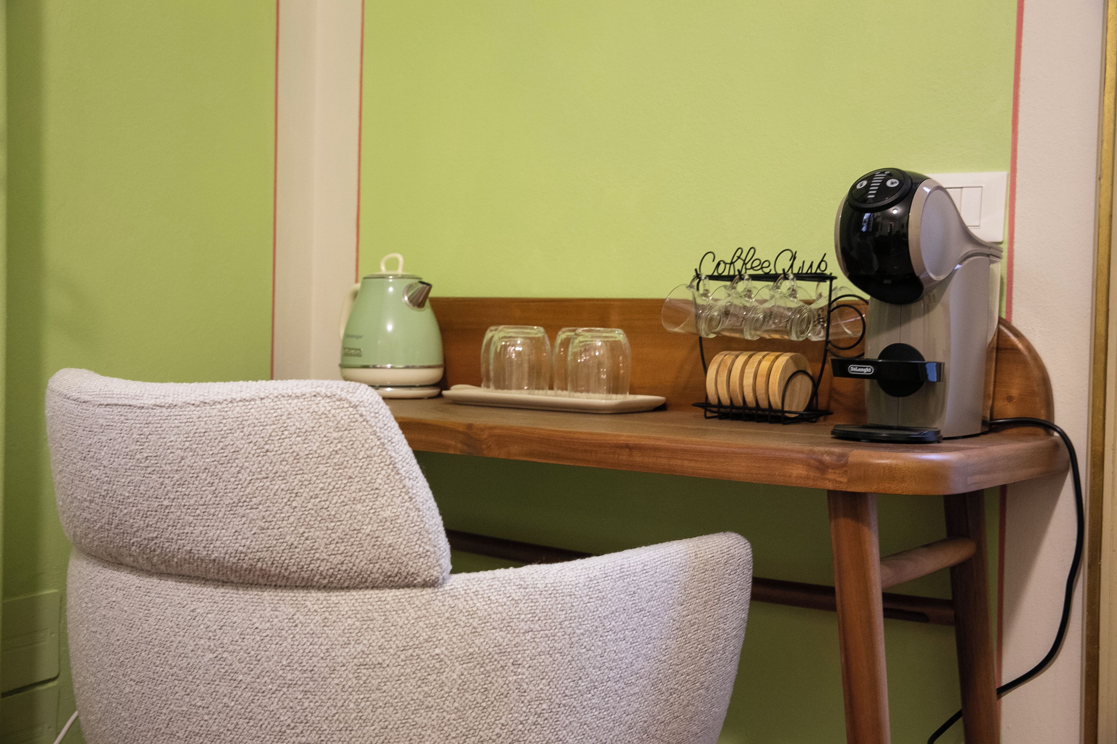 Ein Zimmer mit einem Holztisch, einem grünen Wasserkocher, einer Kaffeemaschine und einem Stuhl.