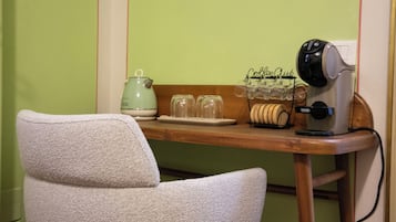 Ein Zimmer mit einem Holztisch, einem grünen Wasserkocher, einer Kaffeemaschine und einem Stuhl.