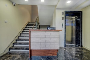 Un vestíbulo de hotel con una escalera de mármol, un mostrador de recepción y un ascensor.