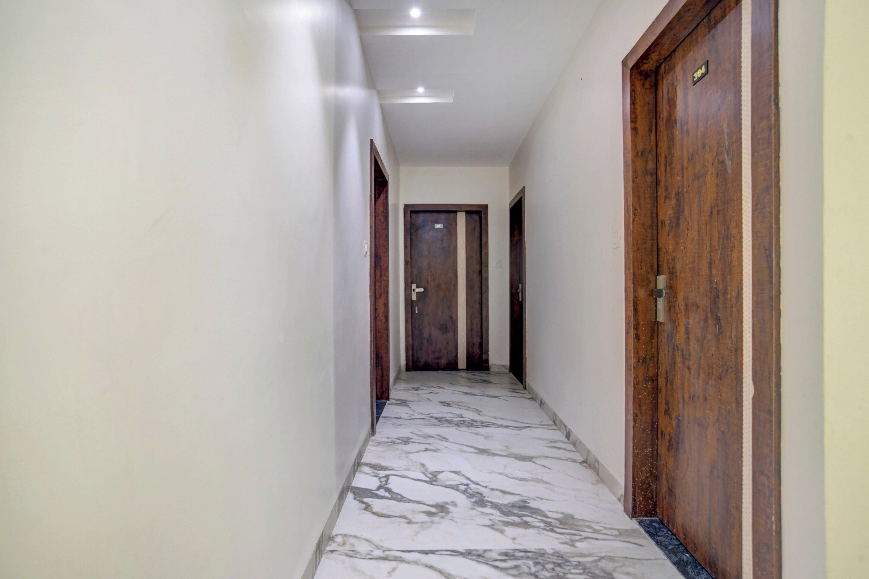 Un pasillo con piso de mármol, puertas de madera e iluminación empotrada en el techo.