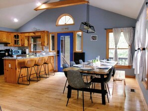 A kitchen with wooden cabinets, a dining area with a table and chairs, and a blue door labeled 'GO HIKE'. - Hawk's View Chalet
with add on Bunkie Rental (Murphy)
