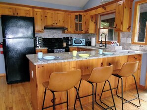 A kitchen with wooden cabinets, a black refrigerator, a microwave, a stove, and bar stools. - Hawk's View Chalet
with add on Bunkie Rental (Murphy)