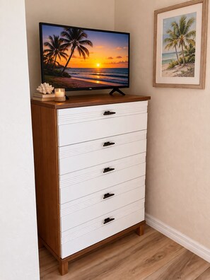 Eine weiße Kommode mit einer Holzplatte und einem Fernseher, der eine Sonnenuntergangsansicht zeigt.