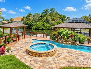 Ein Schwimmbecken mit Steinumrandung, einer Holzterrasse und einem Pavillon.