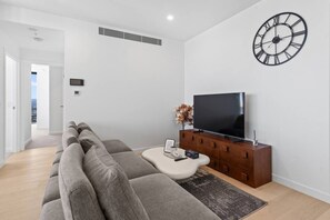 Ein modernes Wohnzimmer mit einem großen Flachbildfernseher, einem Sofa, einem Couchtisch und einer dekorativen Wanduhr.