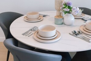 A round dining table with white plates, bowls, and silverware arranged for a meal. - Elegant 2BR with Panoramic Water Views (Broadbeach)