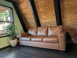 A tan leather sofa against a wooden wall with a window and a potted plant. - Entire chalet in Branson, Missouri (Branson)
