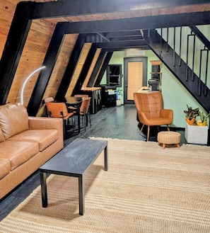 Ein Loftsitzbereich mit hoher Decke, freiliegenden Balken, einem Ledersofa, einem Couchtisch und einem Essbereich mit Stühlen.