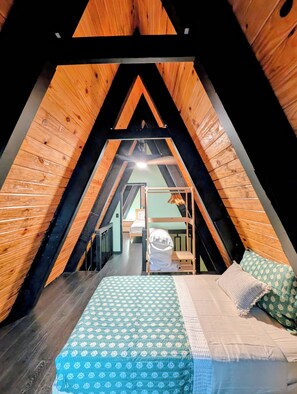 Ein quadratisches Schlafzimmer im Dachgeschoss mit Etagenbett, Holzwänden und geneigter Decke.
