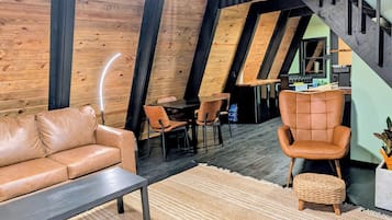 A loft-style room with a wooden ceiling, a leather sofa, a dining table, and a chair.