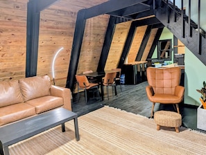 A loft-style room with a wooden ceiling, a leather sofa, a dining table, and a chair. - Entire chalet in Branson, Missouri (Branson)